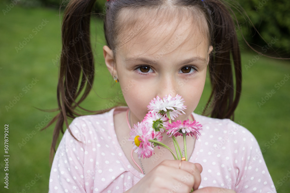 close-up portrait of a cute girl 6-7 years old with a small bouquet of daisies flowers. A little girl with a dreamy look smells flowers. close-up portrait of a cute girl 6-7 years old with a small bouquet of daisies flowers. A little girl with a dreamy look smells flowers.