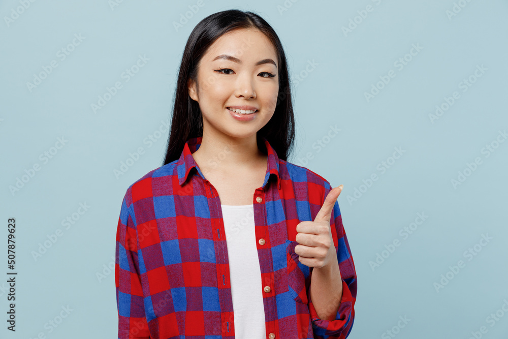 Young smiling satisfied happy fun cool woman of Asian ethnicity 20s wear checkered shirt showing thumb up like gesture isolated on plain pastel light blue color background. People lifestyle concept. Young smiling satisfied happy fun cool woman of Asian ethnicity 20s wear checkered shirt showing thumb up like gesture isolated on plain pastel light blue color background. People lifestyle concept.