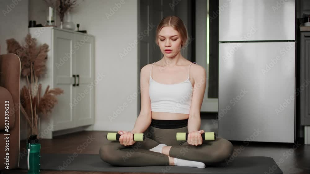 A girl in sportswear performs exercises with dumbbells, sitting on a mat. Sport A girl in sportswear performs exercises with dumbbells, sitting on a mat. Sport