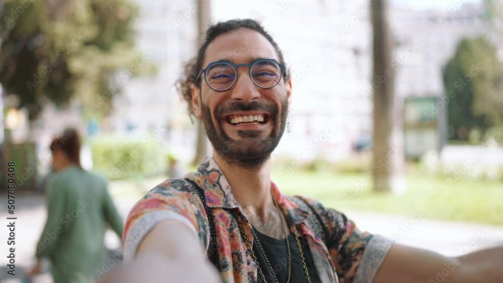 Cheerful curly-haired bearded man in eyeglasses showing peace sign at the camera outdoors Cheerful curly-haired bearded man in eyeglasses showing peace sign at the camera outdoors