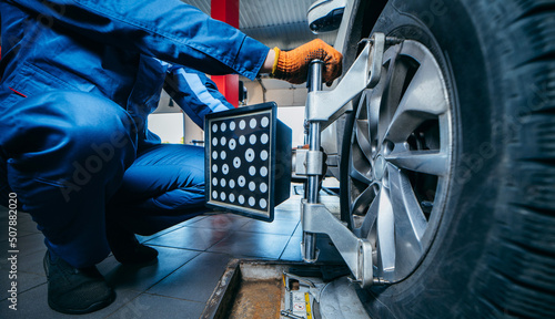 Auto mechanic installing sensor during suspension adjustment and automobile wheel alignment work at repair service station. Close up photo