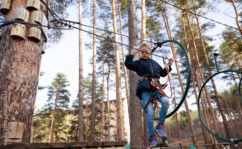 Child using safety equipment at adventure amusement park. Young girl having fun outdoor. Childhood active. Sports extreme activity. Child using safety equipment at adventure amusement park. Young girl having fun outdoor. Childhood active. Sports extreme activity.