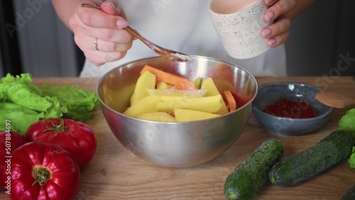 Fototapeta Naklejka Na Ścianę i Meble -  Close-up of a woman preparing vegetables in the kitchen. The hands of an unrecognizable woman sprinkle salt on vegetables in a plate. Cooking in the kitchen.