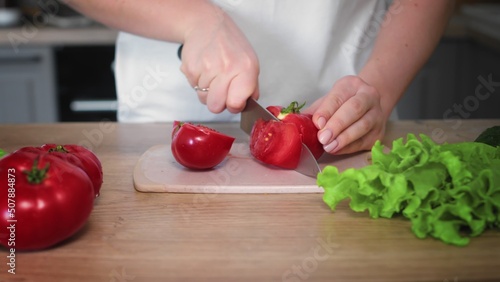 Close-up of an unrecognizable woman's hand cutting a tomato with a kitchen knife. Cooking in the kitchen.