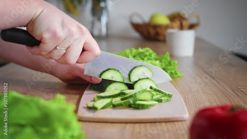Close-up of an unrecognizable woman's hand cutting a cucumber with a kitchen knife. Cooking in the kitchen.
