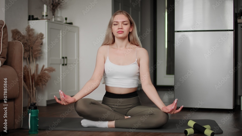 The girl is doing yoga sitting on the floor in the lotus position at home in the living room. Only relaxation and meditation. The girl is doing yoga sitting on the floor in the lotus position at home in the living room. Only relaxation and meditation.