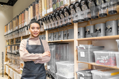 Portrait of african american woman owner of sustainable small local business. Young confident woman wearing apron with crossed hands in local zero waste grocery store
