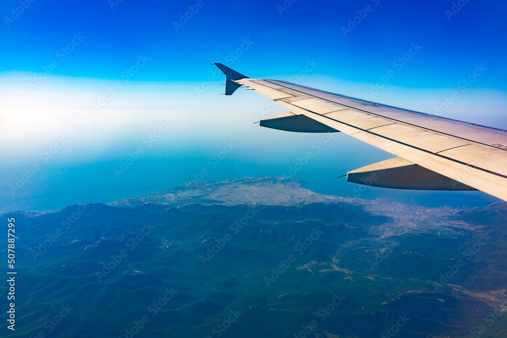 Naklejka premium View from the airplane window at a beautiful blue clear sky, earth, sea and the airplane wing