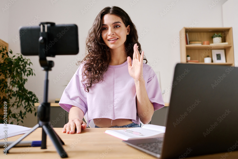 Φωτογραφία Young female blogger sitting at desk in front of smartphone on tripod starting v