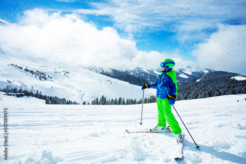 Boy stand on ski track in sport outfit observing the mountain
