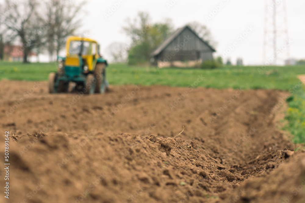 Plowing and sowing the soil with an old farm tractor Belarus in an agricultural field in spring, with old traditional wooden houses Plowing and sowing the soil with an old farm tractor Belarus in an agricultural field in spring, with old traditional wooden houses