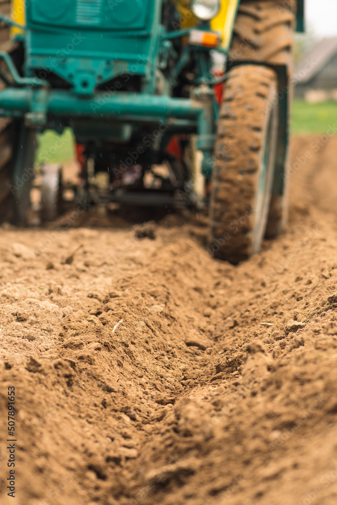 Plowing and sowing the soil with an old farm tractor Belarus in an agricultural field in spring, with old traditional wooden houses Plowing and sowing the soil with an old farm tractor Belarus in an agricultural field in spring, with old traditional wooden houses