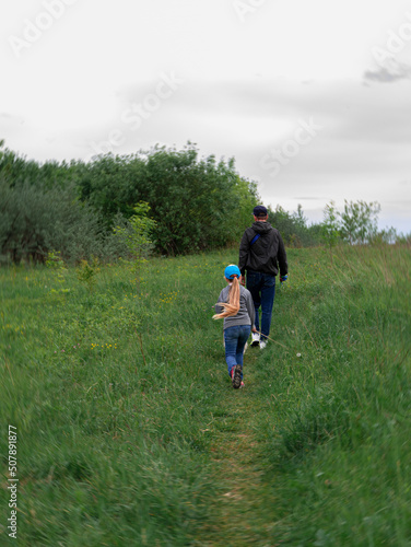 Family walking with dogs on green grass rural landscape. Countryside cottagecore style. Camping activity spring forest. Candid authentic people father and daughter with pets from behind hiking outdoor