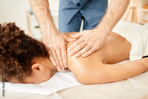 Closeup of male beautician giving back massage to young African American woman enjoying SPA session