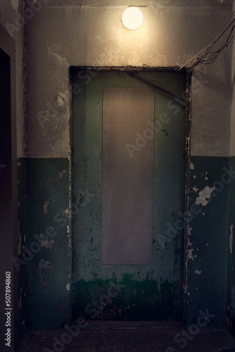 Closed dirty door in the entrance. The light shines over the doorway in a dark room. Abstract interior made of dark concrete. High quality photo © daryakomarova