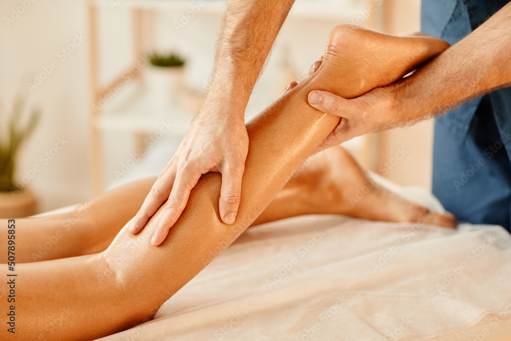 Warm toned closeup of man massaging elegant legs of young woman in SPA session Warm toned closeup of man massaging elegant legs of young woman in SPA session