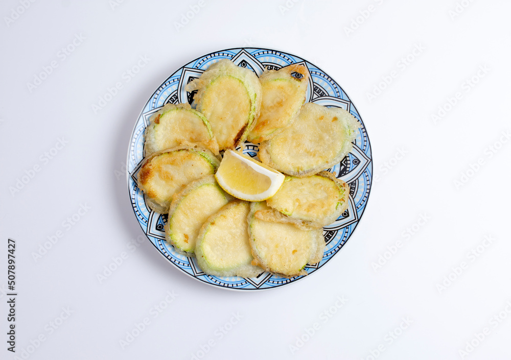 Tasty fried zucchini with lemon on plate, top view, isolated on white background
