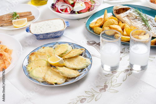 Greek food background. Ouzo, zucchini, Greek salad, tzatziki, assortment of feta. Roasted dorado  Top view. Traditional Greek taverna menu. Close up photo