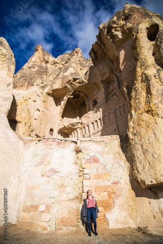 Young happy woman traveler enjoying a vacation in desert Cappadocia Turkey. Tourist blonde girl in glasses and pink shirt outdoor portrait. Sunny female portrait in the desert ancient stone ruins