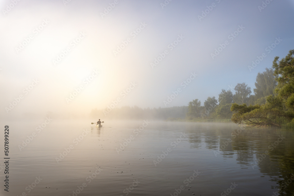 Silhouette of a man in a boat. Mystical landscape. Fog in the early morning on the river. The trees near the water are illuminated by the rays of the rising sun. Silhouette of a man in a boat. Mystical landscape. Fog in the early morning on the river. The trees near the water are illuminated by the rays of the rising sun.