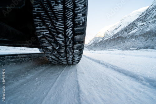 View from the bottom of the car on a snowy road where you can see the tread of a winter tire in the snow © Rolands