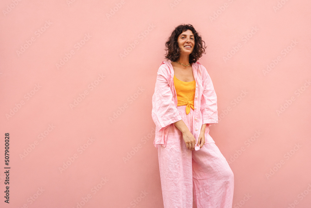 Beautiful young caucasian woman is smiling looking into camera on pink background with place for text. Brunette with bob haircut wears summer shirt and pants. Happy weekend concept. Beautiful young caucasian woman is smiling looking into camera on pink background with place for text. Brunette with bob haircut wears summer shirt and pants. Happy weekend concept.