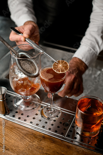 close-up view on glass with drink which hand of bartender decorates with a dry slice of lemon