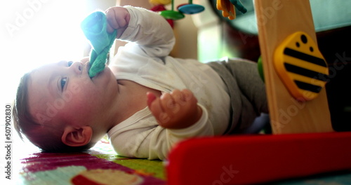 Fotografie, Obraz Baby infant lying on floor on play mat putting sock cloth in mouth, child toddle