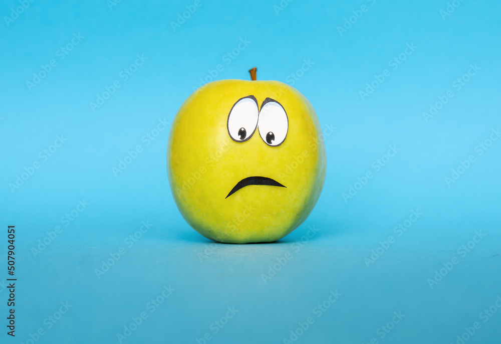 Fototapeta premium negative emotions from fear to panic, sad Face on an apple - abstract image of human emotions on blue background