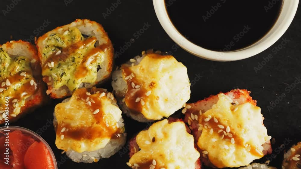 Baked rolls in teriyaki sauce with sesame seeds on a black board next to wasabi and pickled ginger Baked rolls in teriyaki sauce with sesame seeds on a black board next to wasabi and pickled ginger