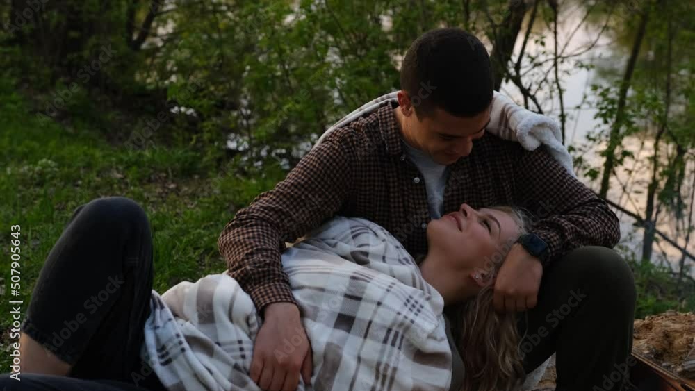 Attractive couple relaxing in the forest on a sunny day, man kissing girlfriend lying in his knees. Camping love story. Attractive couple relaxing in the forest on a sunny day, man kissing girlfriend lying in his knees. Camping love story.