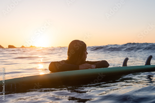 Fototapeta Naklejka Na Ścianę i Meble -  Surfer girl waiting for a wave in the water at sunset