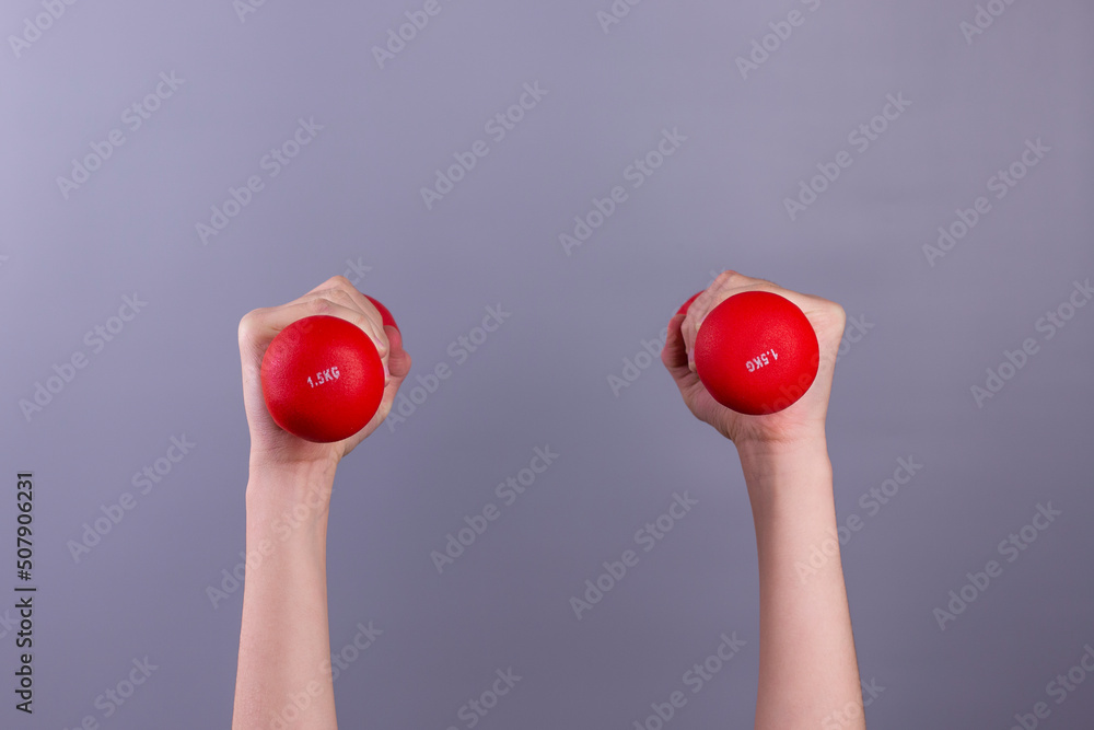 Girl 's hands holding red dumbbells on grey background. concept. Sport and healthy lifestyle concept with Copy space. Girl 's hands holding red dumbbells on grey background. concept. Sport and healthy lifestyle concept with Copy space.
