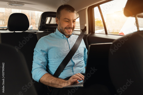 Businessman using laptop while going by car © Prostock-studio
