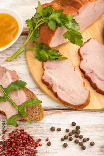Smoked pork ham on cutting board on white wooden background. Side view, close up, selective focus.