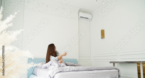 beautiful woman relaxing in bed and turning on air conditioner
