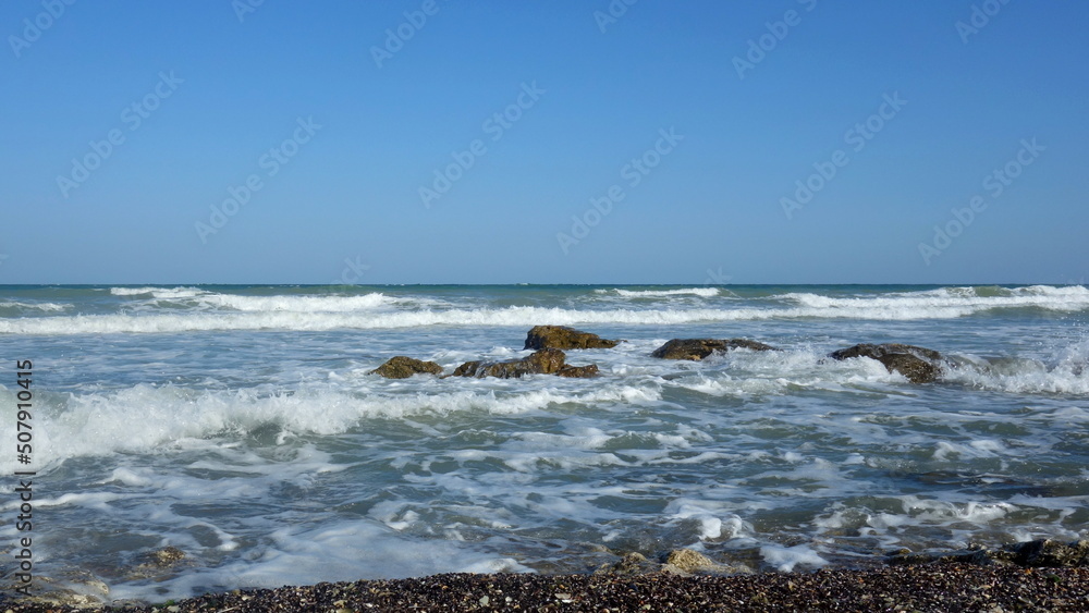 The Black Sea near Vama Veche in Romania. Steady waves coming towards shore full of shells and a few rocks in the water. 
