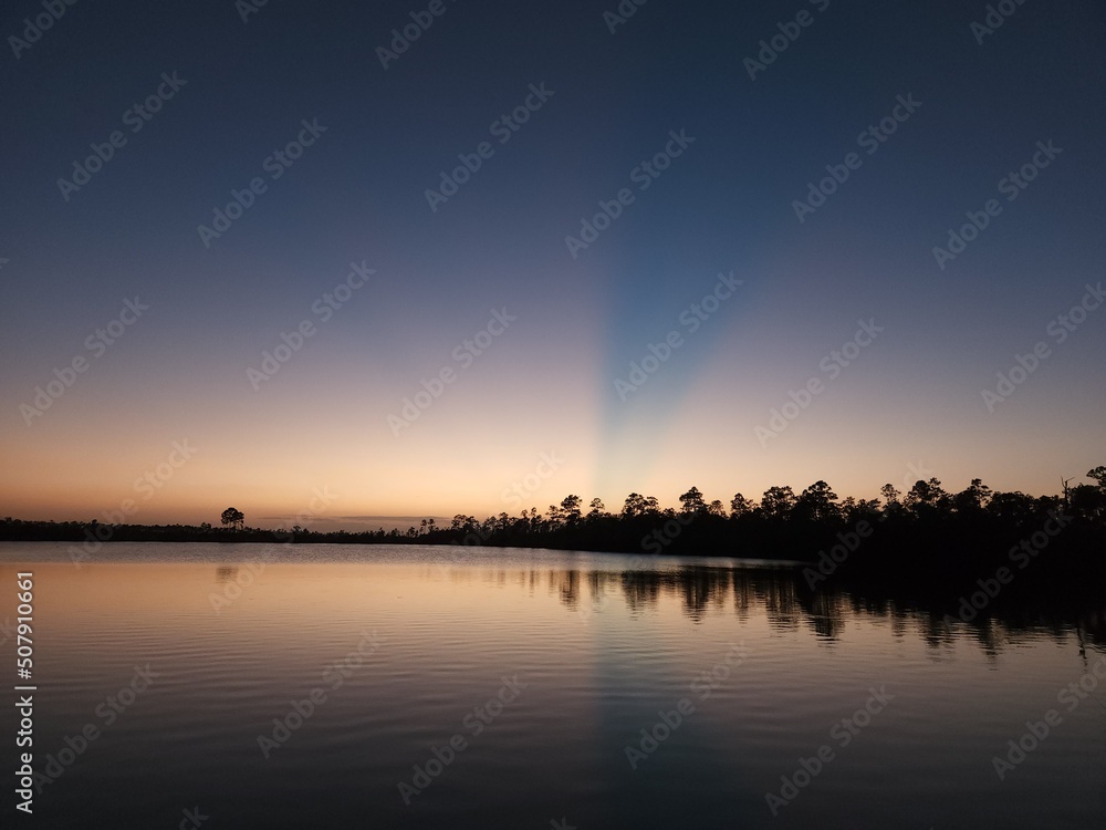 Sun rays in twilight over Pine Glades Lake in Everglades National Park, Florida on calm clear April evening.