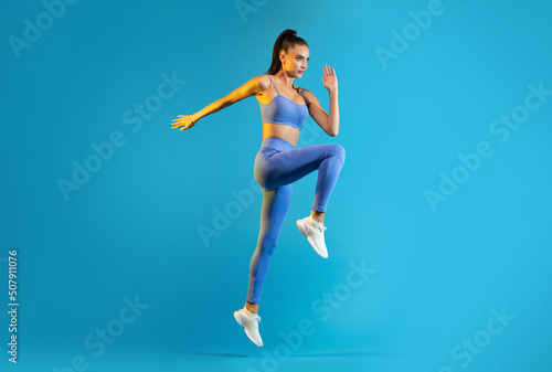 Fototapeta Naklejka Na Ścianę i Meble -  Sportswoman Exercising Doing Elbow To Knee Crunch Over Blue Background