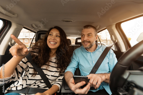 Happy couple driving car and using cell phone © Prostock-studio