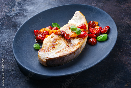 Fried swordfish steak with tomatoes and paprika served as close-up on a design plate photo