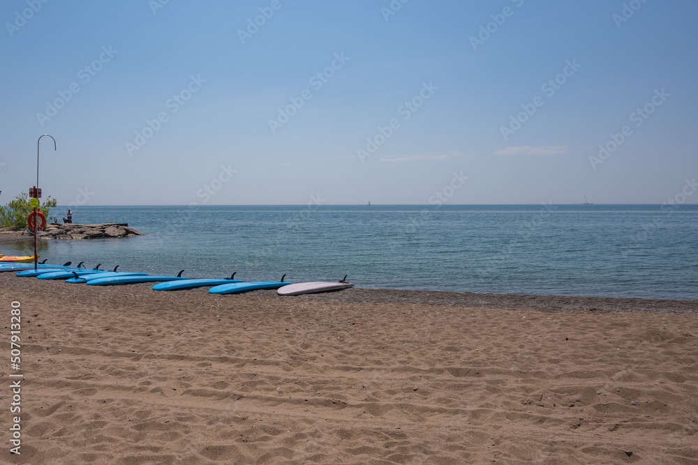 Stand Up Papple Boards (SUPS) arrayed on a Lake Ontario beach and available for rental. Room for text