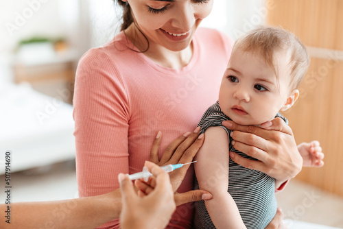 Vaccination concept. Pediatrician doctor giving vaccine shot to little baby at home, making injection for infant child photo