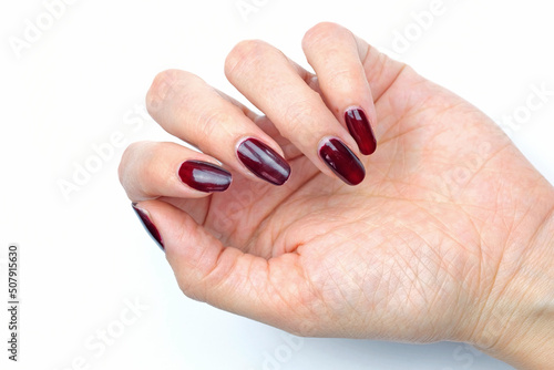 Girls hand with long burgundy nails closeup. Girls wrist on a white background. Manicure with long dark polished nails.