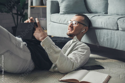 Man with wireless headphones using gadgets, talking and smiling while lying on the floor. Internet technology. Business portrait.