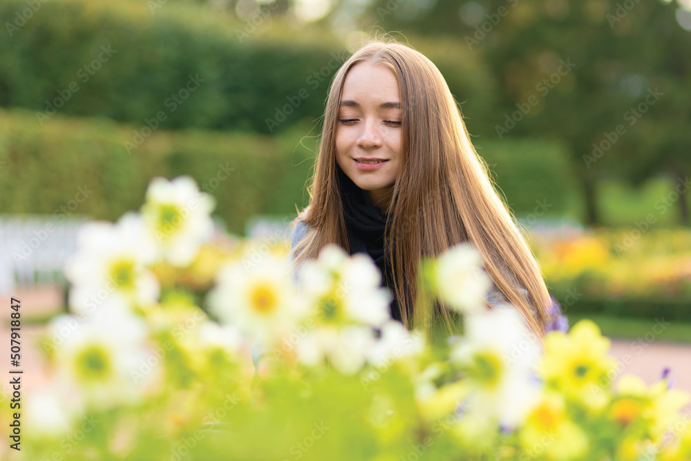 smiling girl with long hair smelling flowers in a flowerbed in the park, garden. smiling girl with long hair smelling flowers in a flowerbed in the park, garden.