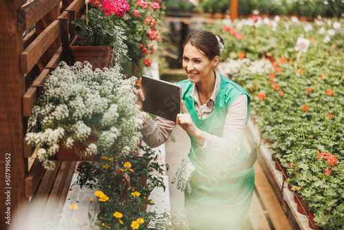 Florist Using Digital Tablet While Caring About Flowers In Garden Center