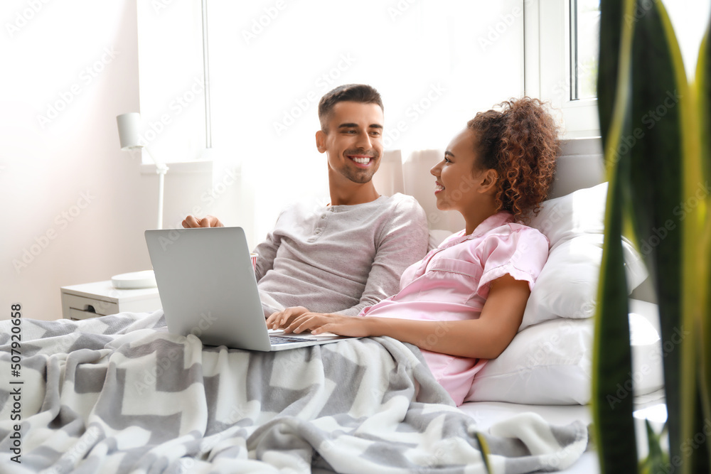 Young couple with popcorn watching movie on laptop in bed Young couple with popcorn watching movie on laptop in bed