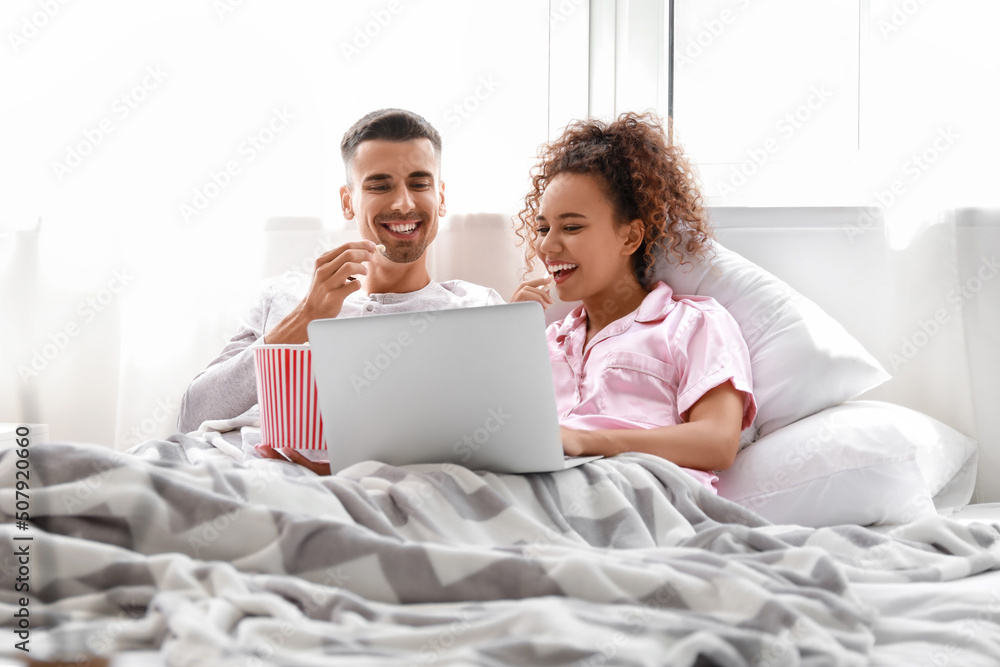 Young couple with popcorn watching movie on laptop in bed Young couple with popcorn watching movie on laptop in bed