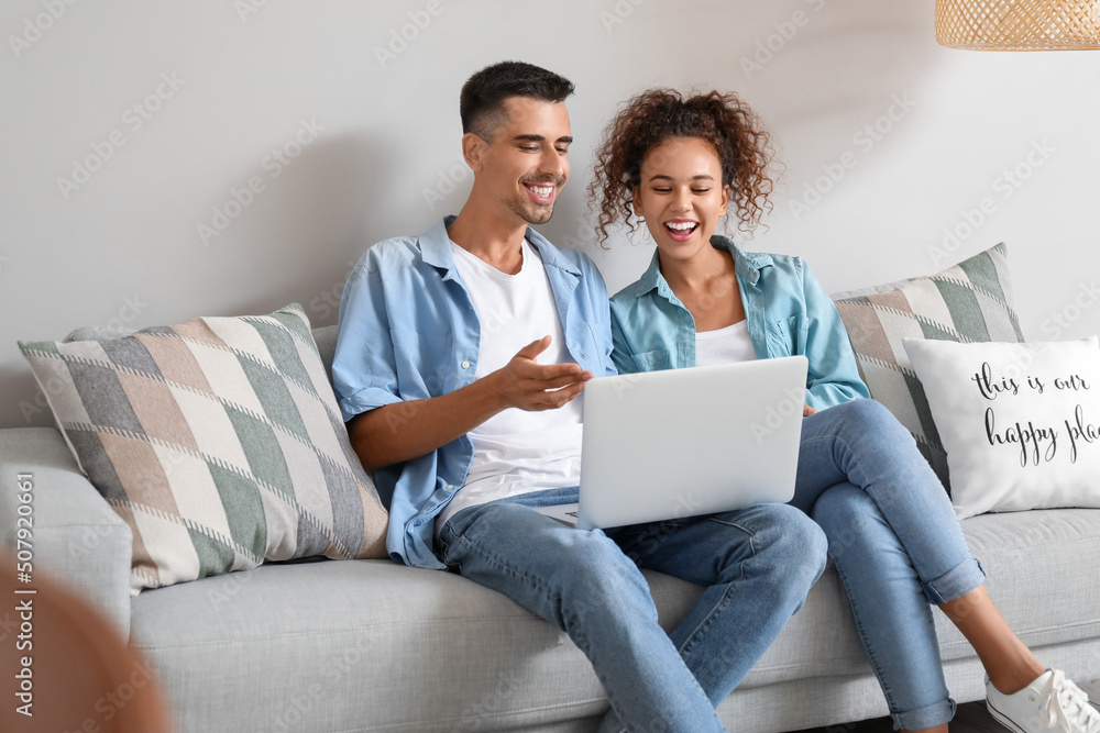 Young couple with laptop video chatting on sofa at home